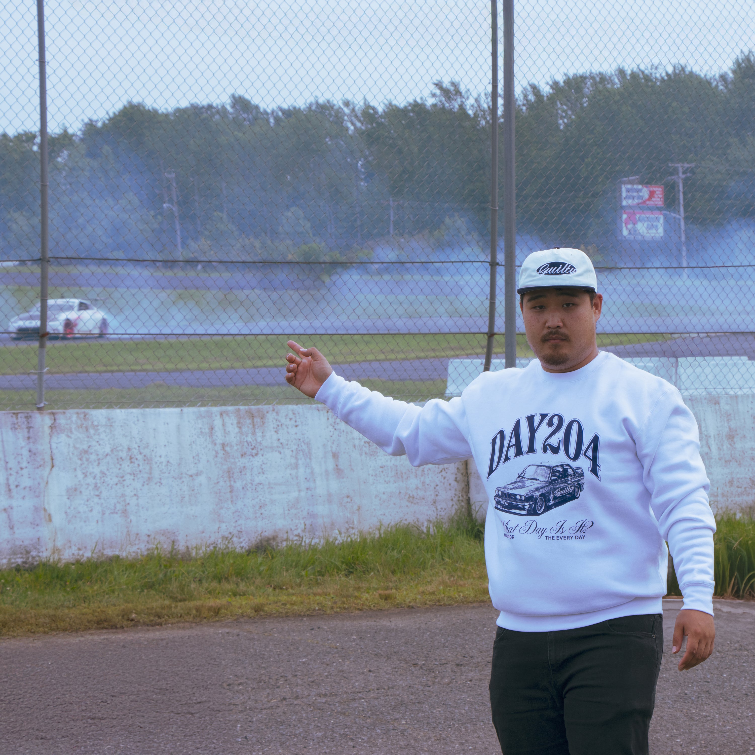 Man wearing a white sweatshirt with 'DAY204' text and graphic, standing on a track.