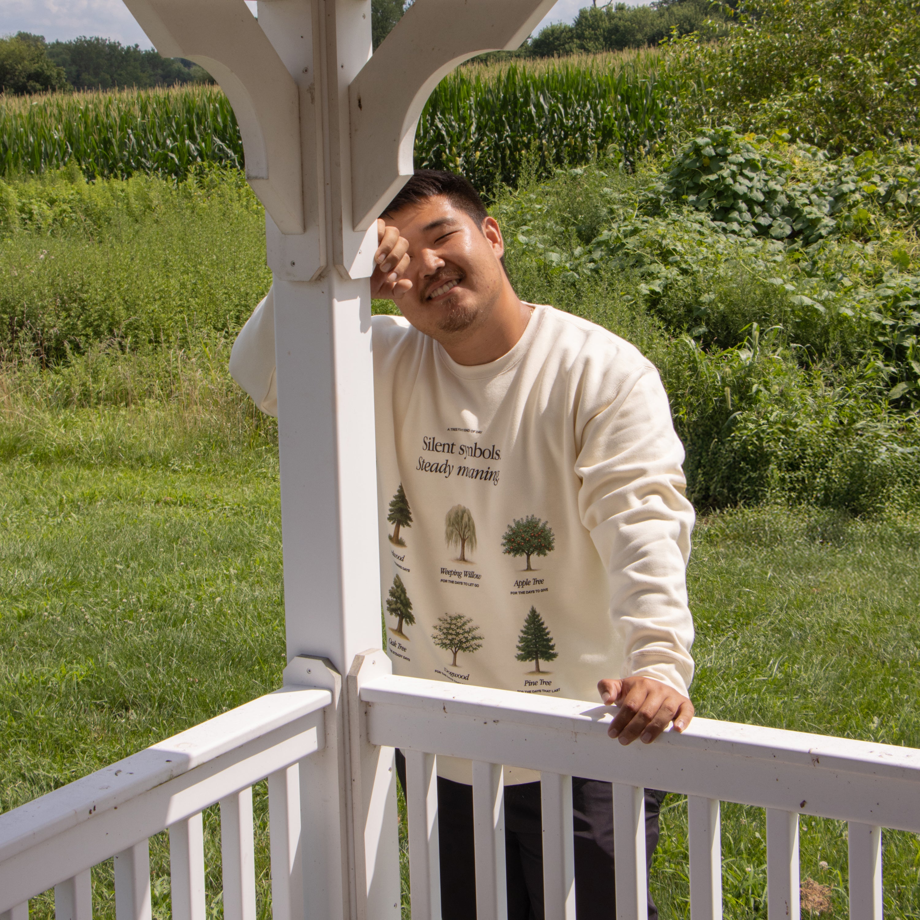 Man wearing a beige sweatshirt with tree design standing in a field