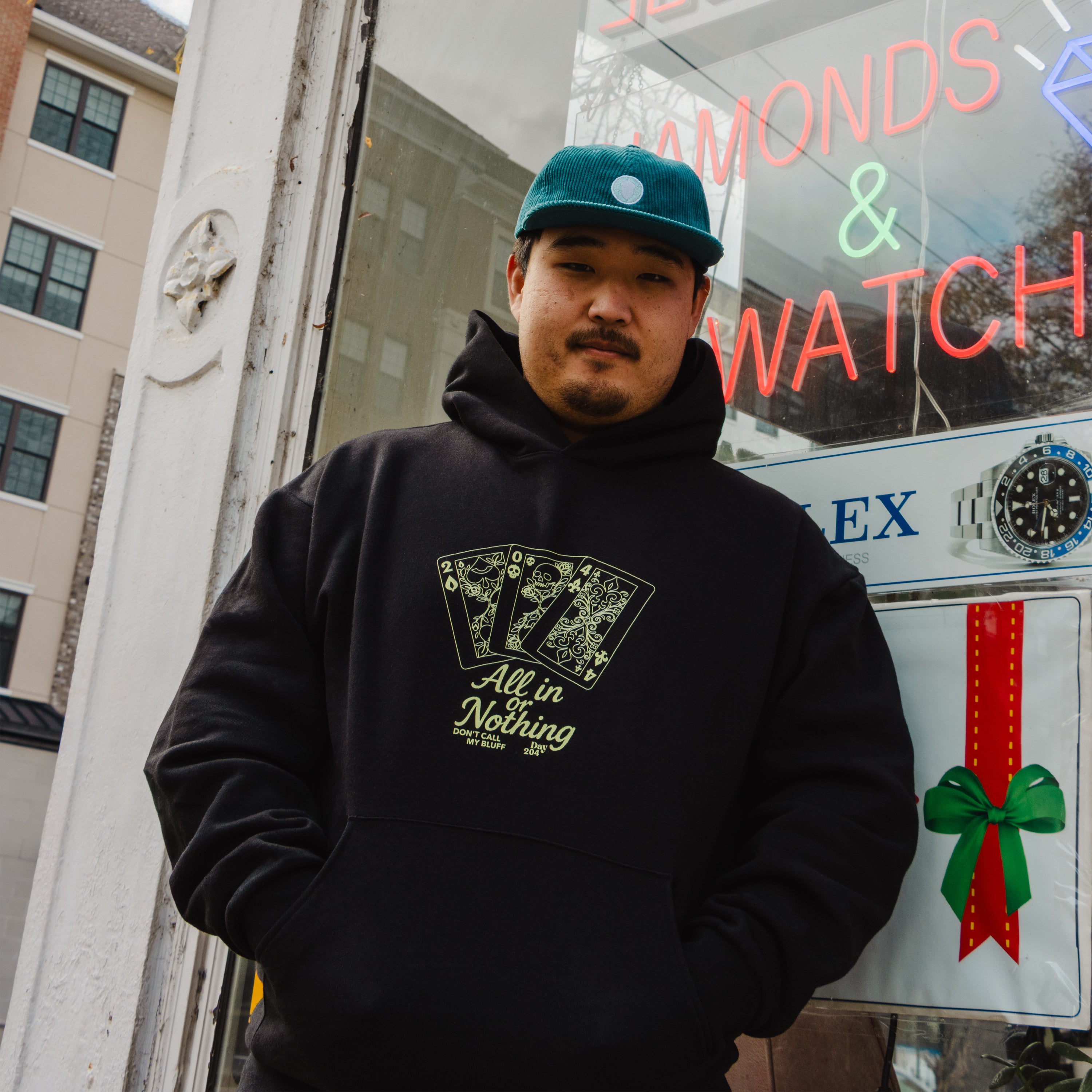 Man wearing a black hoodie with a graphic design in front of a store window.