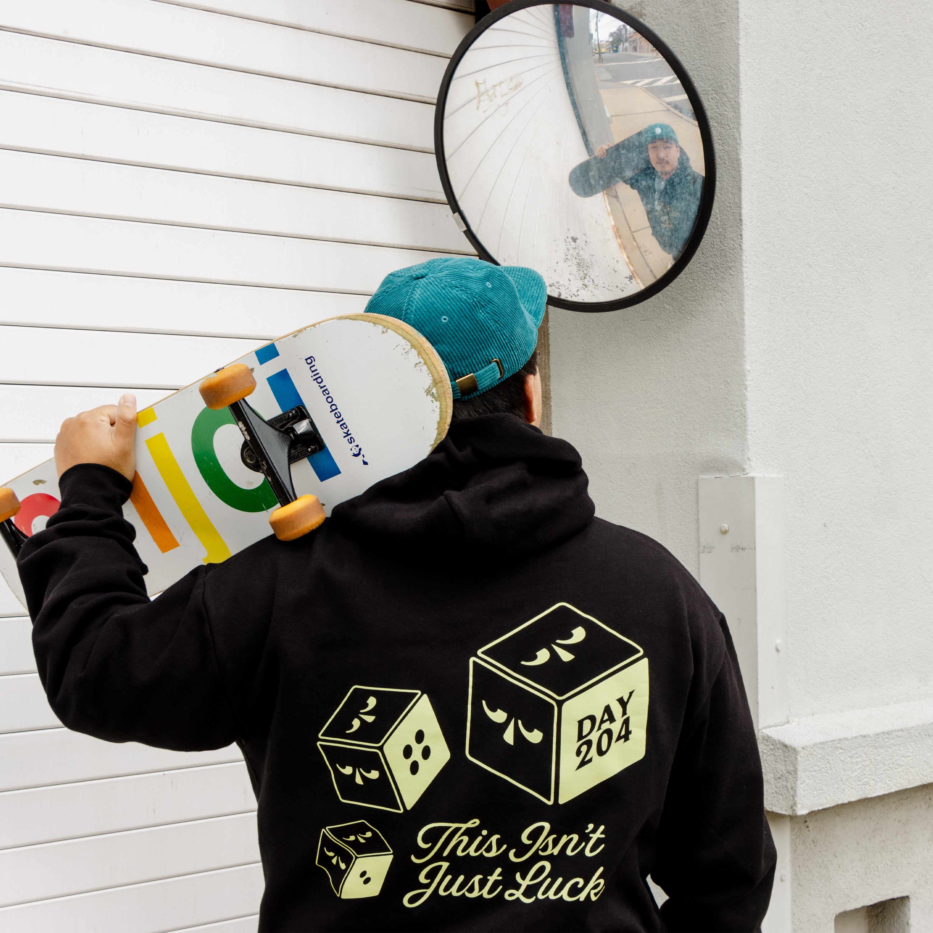 Person holding a skateboard with a mirror reflection, wearing a black hoodie with text and graphics.