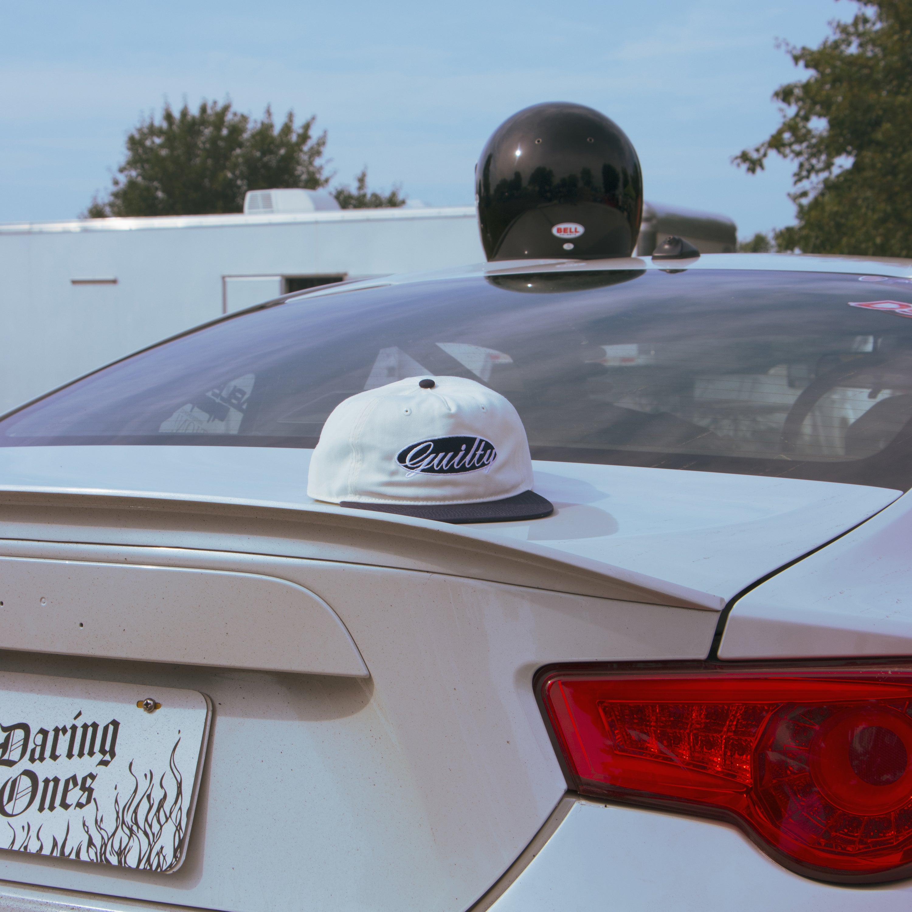 Car with a helmet on the roof and a cap with 'Guilty' branding on the trunk.