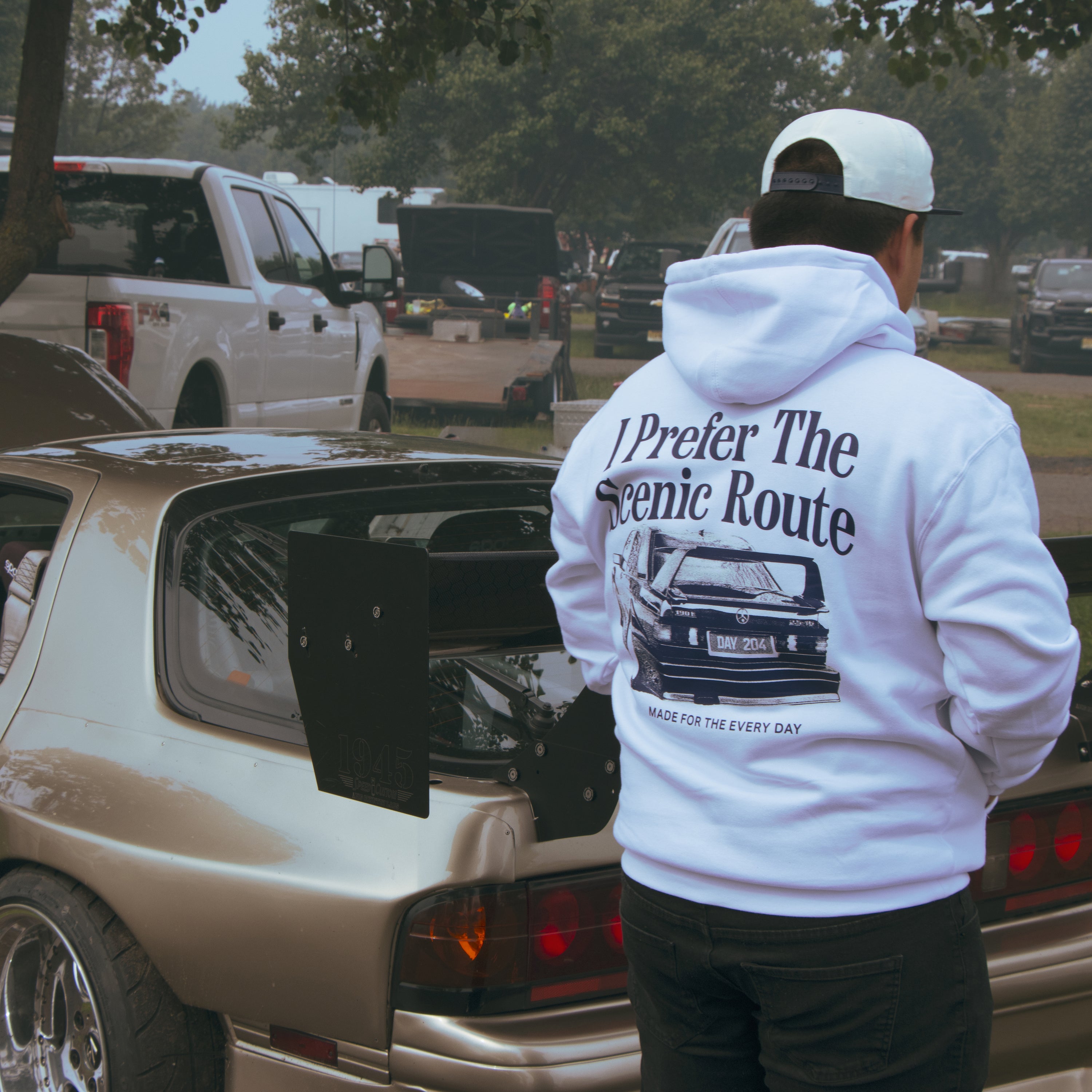 Person wearing a hoodie with text and graphics, standing next to an open car hood.