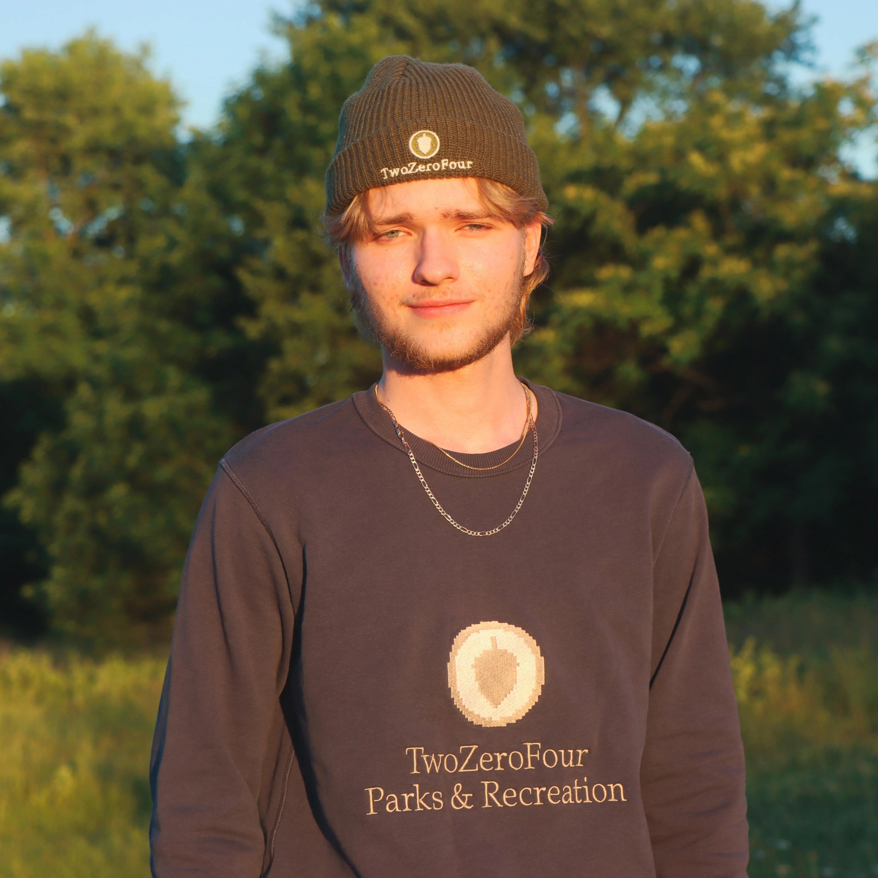 Man wearing a 'TwoZeroFour Parks & Recreation' sweatshirt and beanie in a natural setting