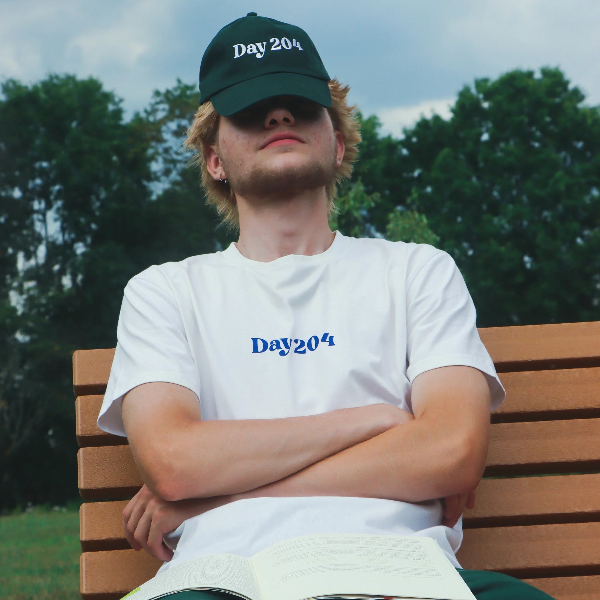 Person sitting on a bench wearing a 'Day 204' cap and t-shirt in an outdoor setting.