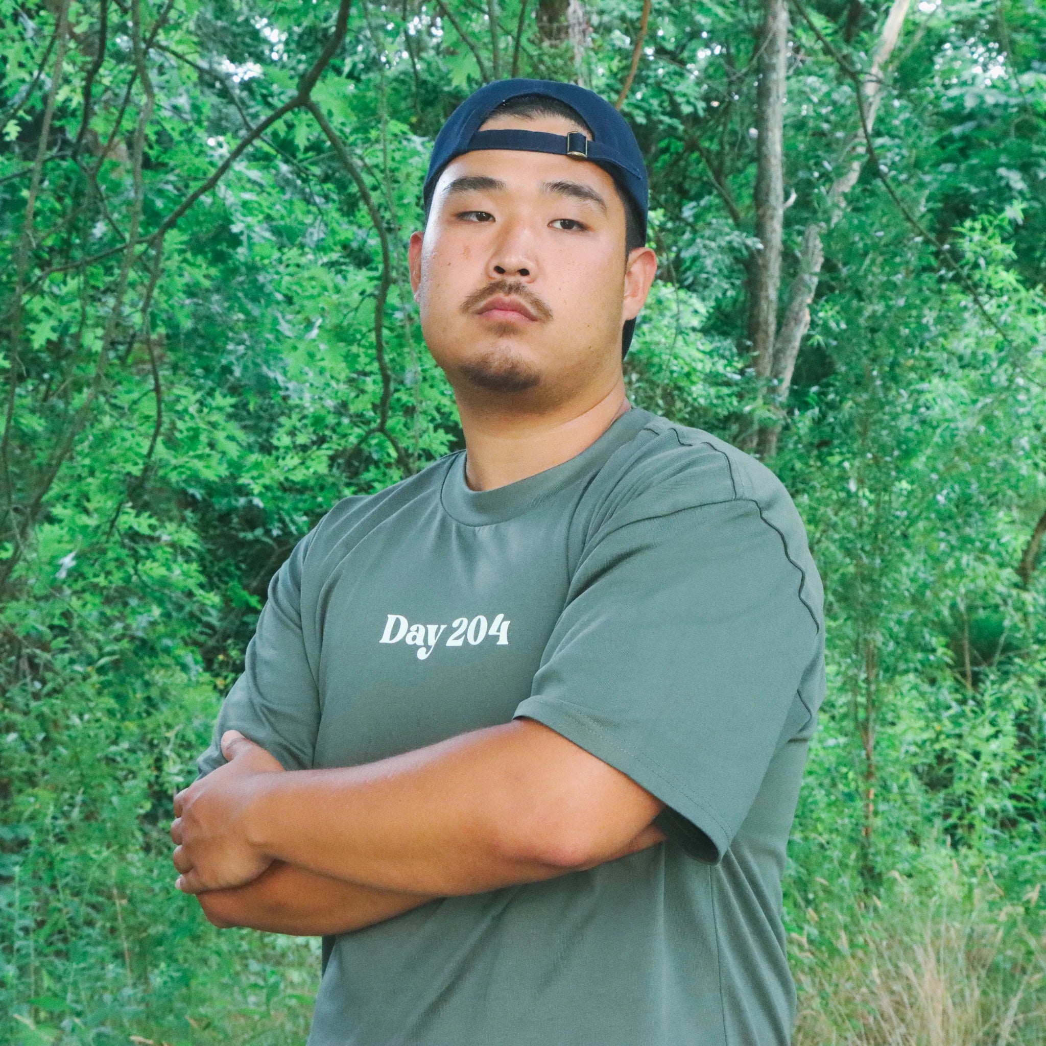 Man wearing a green 'Day 204' t-shirt standing in a forest.