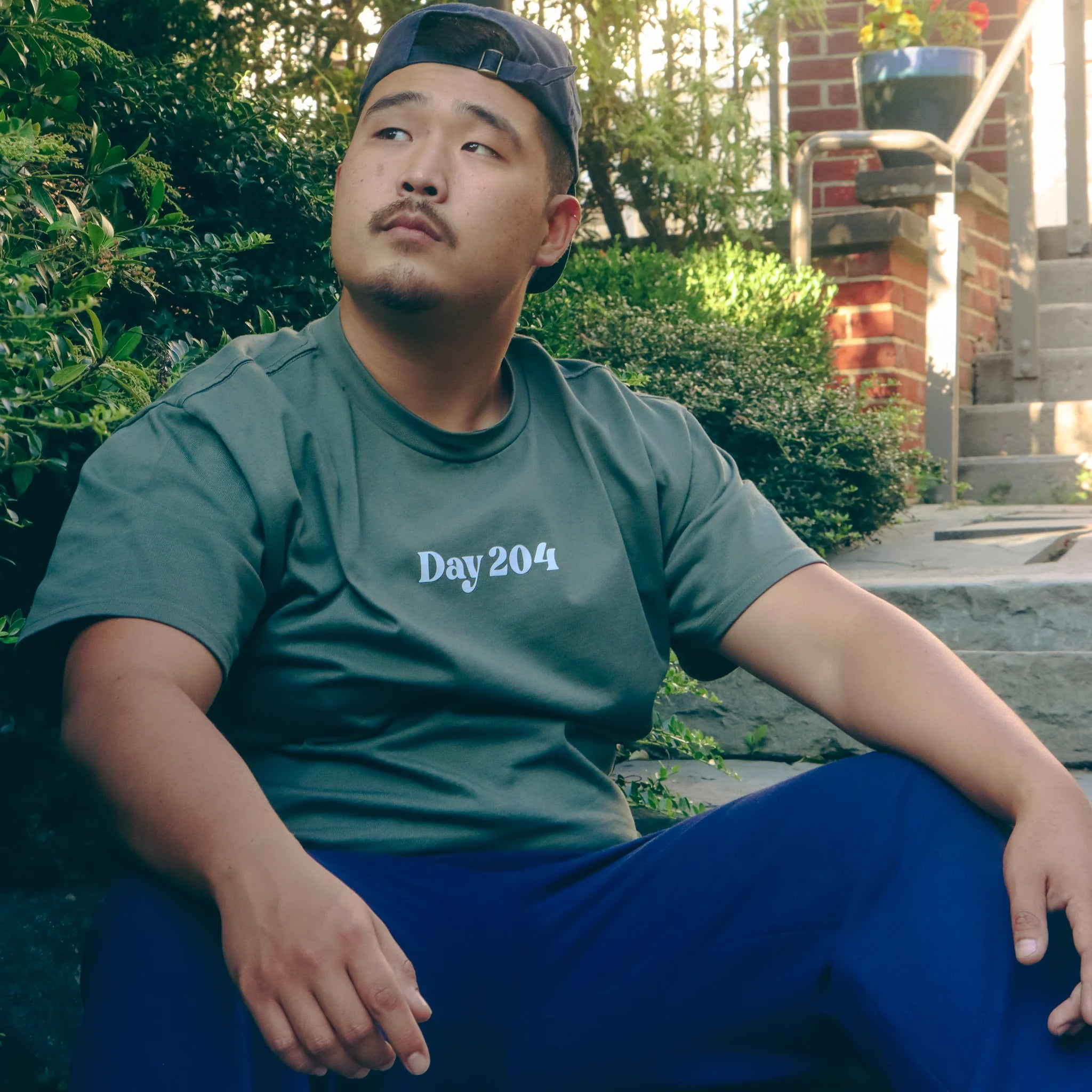 Man wearing a green t-shirt with 'Day 204' text, sitting outdoors.