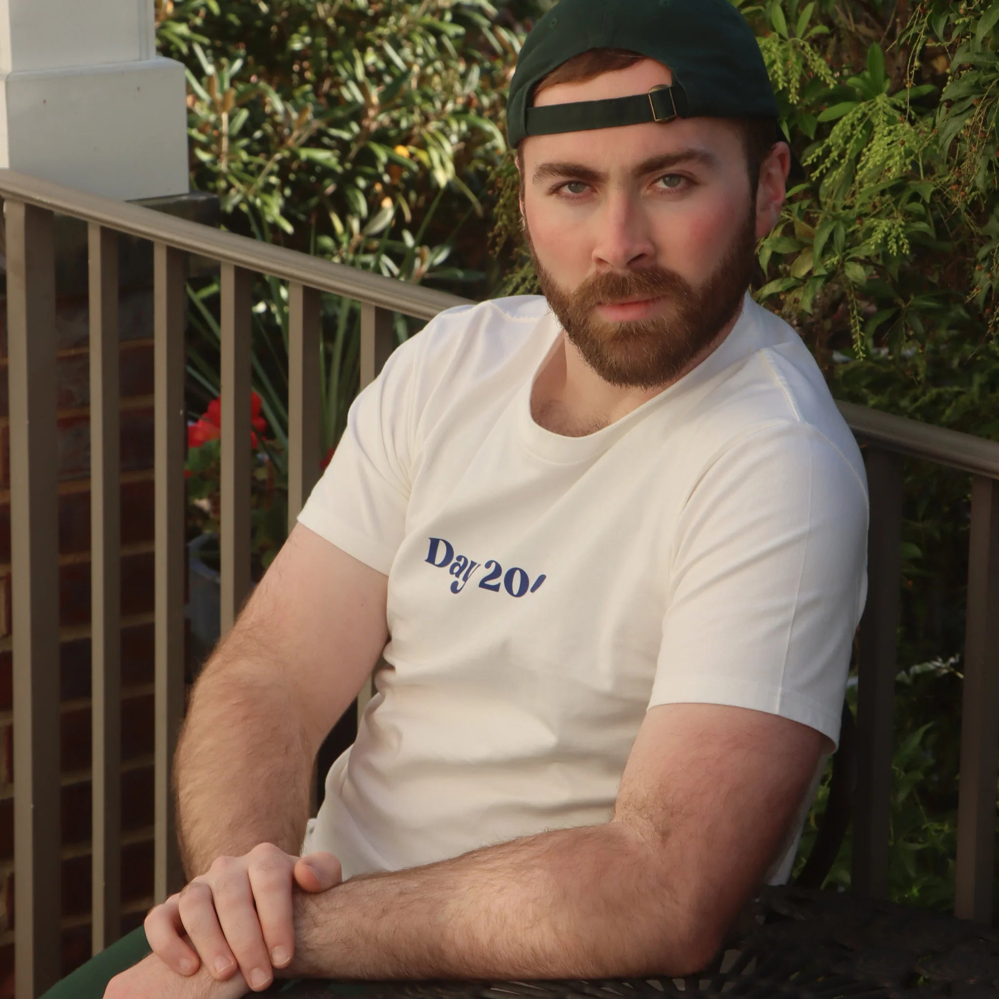 Man wearing a white t-shirt with 'Day 204' text, sitting outdoors.
