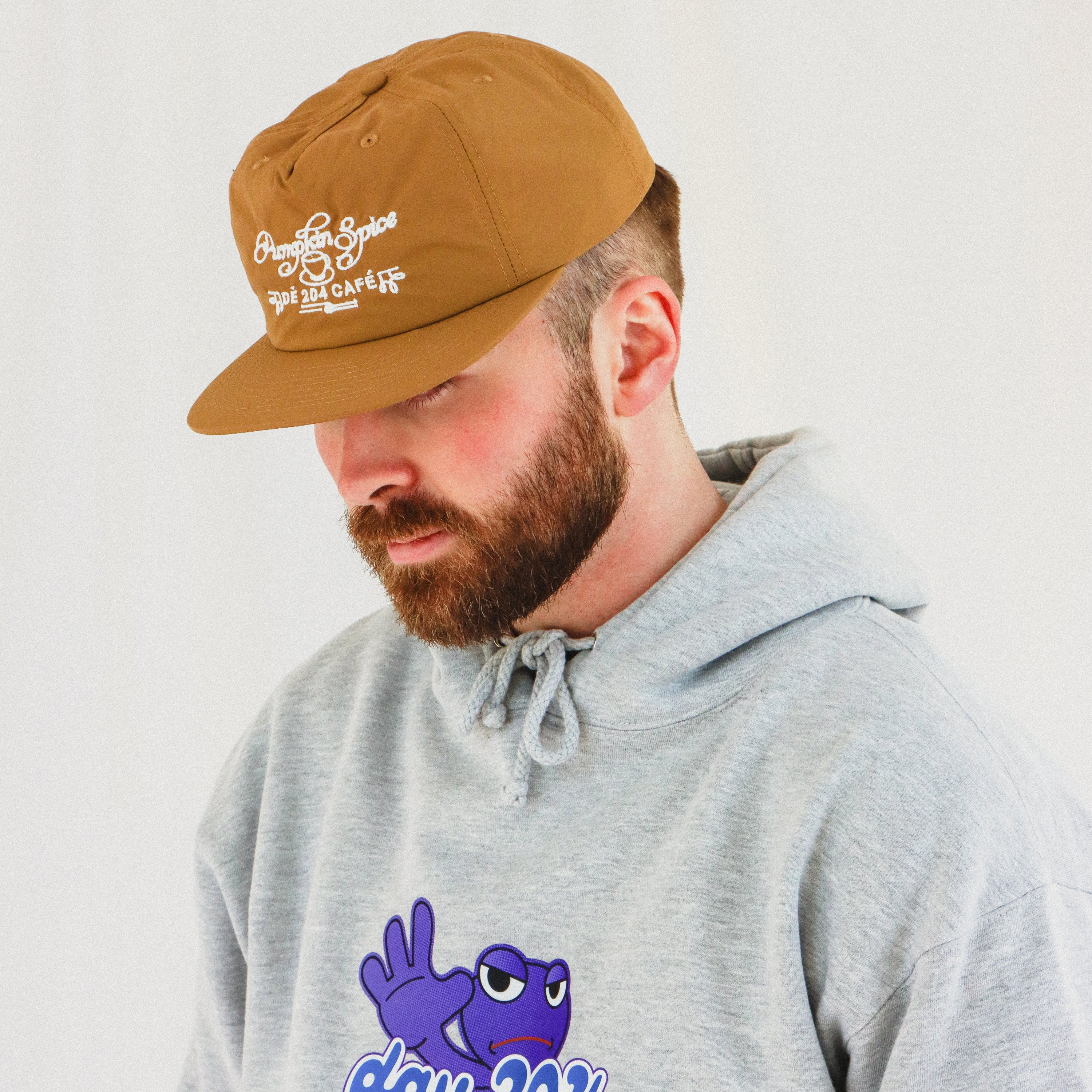 Man wearing a brown cap and gray hoodie with a blue character design on a plain background